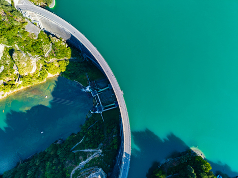 Aerial view of Barrage de Rossens dam curving across the turquoise waters of Lac de la Gruyere surrounded by lush green forests in Pont la Ville Fribourg Switzerland.