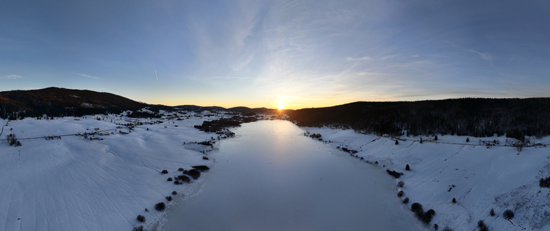 Aerial view of a frozen lake reflecting the vibrant sunset bordered by snow covered landscapes and dark forests Les Rousses Bourgogne Franche Comté France. Aerial view of a frozen lake reflecting the vibrant sunset bordered by snow covered landscapes and dark forests Les Rousses Bourgogne Franche Comté France.