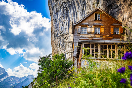 View of a rustic wooden house clinging precariously to a sheer cliff face amidst vibrant greenery against a backdrop of snow capped mountains Schwende Rüte Switzerland. View of a rustic wooden house clinging precariously to a sheer cliff face amidst vibrant greenery against a backdrop of snow capped mountains Schwende Rüte Switzerland.