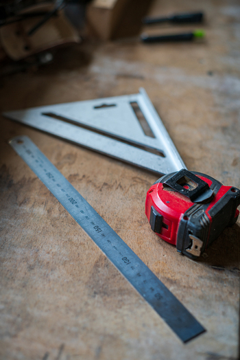 View of a metal ruler a triangle square and a red tape measure resting on a wooden workbench in Looe Cornwall United Kingdom. View of a metal ruler a triangle square and a red tape measure resting on a wooden workbench in Looe Cornwall United Kingdom.