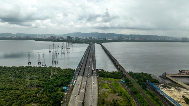 Aerial view of Vashi Bridge spanning Thane Creek with traffic lush mangroves power transmission towers and city skyline in Navi Mumbai Maharashtra India.