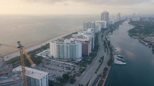 Aerial view of Miami Beach featuring high rise buildings along the coast a construction crane a waterway with yachts and palm lined roads in Miami Beach Florida United States. Aerial view of Miami Beach featuring high rise buildings along the coast a construction crane a waterway with yachts and palm lined roads in Miami Beach Florida United States.