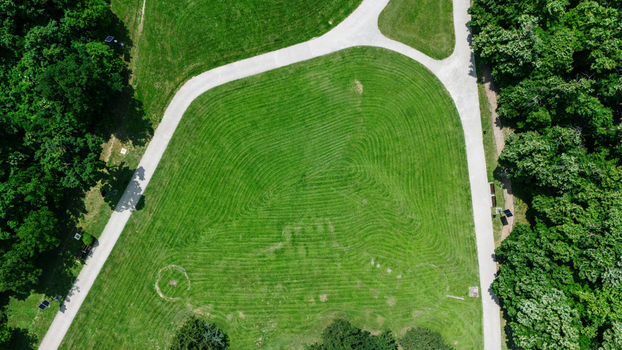 Aerial view of a manicured green lawn with mowed patterns surrounded by lush forest trees and a winding white pedestrian path in Novi Sad Vojvodina Serbia. Aerial view of a manicured green lawn with mowed patterns surrounded by lush forest trees and a winding white pedestrian path in Novi Sad Vojvodina Serbia.