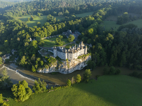 Aerial view of the historic Chateau de Walzin perched on a rocky cliff above the Lesse river surrounded by lush forest and green meadows in Dinant Region wallonne Belgium.