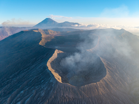 Aerial view of Mount Bromo crater with volcanic smoke rising from the rugged landscape under a clear blue sky in Tosari East Java Indonesia.