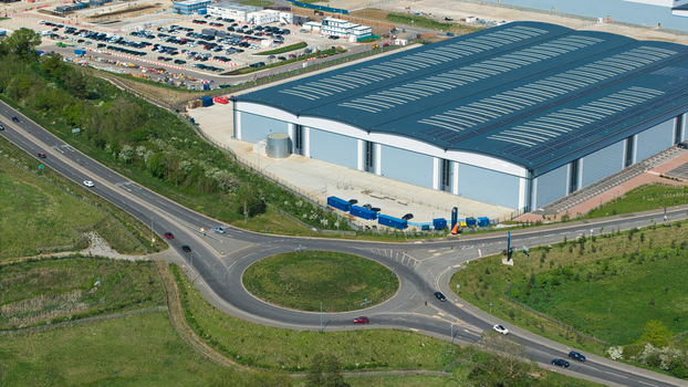 Aerial view of Symmetry Park distribution center featuring a large modern warehouse a busy roundabout and extensive parking facilities in Kettering England United Kingdom. Aerial view of Symmetry Park distribution center featuring a large modern warehouse a busy roundabout and extensive parking facilities in Kettering England United Kingdom.