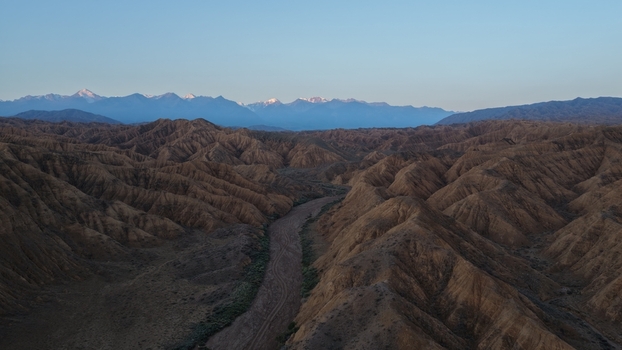 Aerial view of the rugged arid canyons and rolling hills with snow capped mountains visible in the distance under a clear sky Issyk Kul Region Kyrgyzstan. Aerial view of the rugged arid canyons and rolling hills with snow capped mountains visible in the distance under a clear sky Issyk Kul Region Kyrgyzstan.
