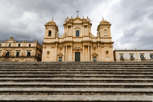 View of the Noto Cathedral with its grand stone staircase and baroque facade under a cloudy sky in Noto Sicily Italy. View of the Noto Cathedral with its grand stone staircase and baroque facade under a cloudy sky in Noto Sicily Italy.