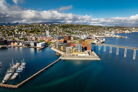 Aerial view of modern waterfront buildings the Tromso Bridge a marina with moored boats and the surrounding mountainous landscape in Tromso Troms Norway.