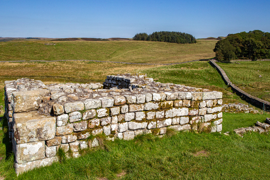 View of the ancient stone ruins of Vindolanda Roman fort set against rolling green hills and a clear blue sky in Hexham England United Kingdom. View of the ancient stone ruins of Vindolanda Roman fort set against rolling green hills and a clear blue sky in Hexham England United Kingdom.