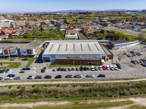 Aerial view of a modern building with a bright roof surrounded by cars and green land against a distant cityscape Ilhavo Aveiro Portugal. Aerial view of a modern building with a bright roof surrounded by cars and green land against a distant cityscape Ilhavo Aveiro Portugal.