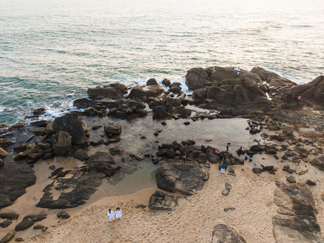 Aerial view of people walking on a sandy beach and rocky shoreline with tide pools and ocean waves in Galle Southern Province Sri Lanka. Aerial view of people walking on a sandy beach and rocky shoreline with tide pools and ocean waves in Galle Southern Province Sri Lanka.