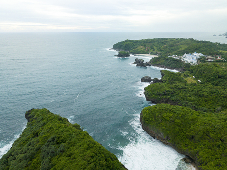 Aerial view of lush green cliffs meeting the turquoise sea with white buildings nestled along the coast Jungwok Beach Gunungkidul Regency Special Region of Yogyakarta Indonesia. Aerial view of lush green cliffs meeting the turquoise sea with white buildings nestled along the coast Jungwok Beach Gunungkidul Regency Special Region of Yogyakarta Indonesia.