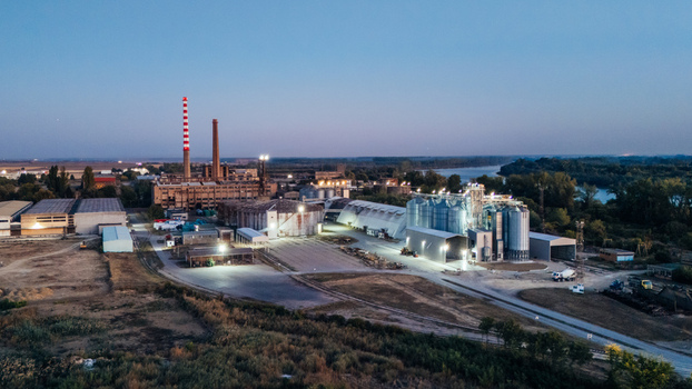 Aerial view of an industrial grain processing facility with tall silos a striped chimney and storage buildings along the Sava River at twilight in Sremska Mitrovica Vojvodina Serbia.