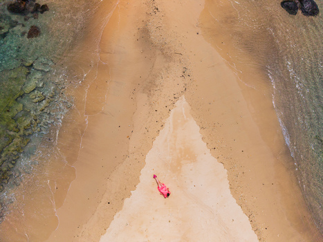 Aerial view of a person in red standing on a sandy beach where turquoise waters meet the shore Vista do Mar Mahe Island Seychelles. Aerial view of a person in red standing on a sandy beach where turquoise waters meet the shore Vista do Mar Mahe Island Seychelles.