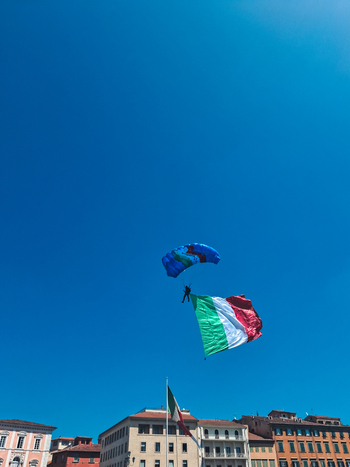 Pisa Italy 27 April 2026 View of a skydiver descending with a large Italian flag against a clear blue sky above the historic buildings of Pisa. Pisa Italy 27 April 2026 View of a skydiver descending with a large Italian flag against a clear blue sky above the historic buildings of Pisa.