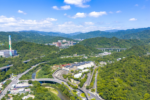 Aerial view of the lush green hills and urban infrastructure in Taipei featuring a river winding roads and a prominent industrial chimney under a bright blue sky in Taipei Taipei City Taiwan. Aerial view of the lush green hills and urban infrastructure in Taipei featuring a river winding roads and a prominent industrial chimney under a bright blue sky in Taipei Taipei City Taiwan.