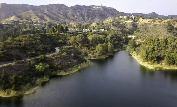 Aerial view of the Hollywood Reservoir with the iconic Hollywood sign visible on the hills in the background surrounded by lush greenery and trees in Hollywood California United States. Aerial view of the Hollywood Reservoir with the iconic Hollywood sign visible on the hills in the background surrounded by lush greenery and trees in Hollywood California United States.