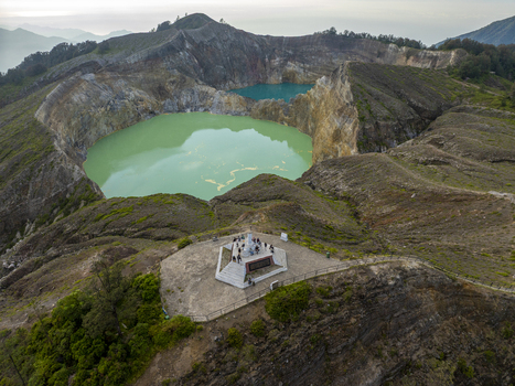 Aerial view of the vibrant green and turquoise crater lakes of Kelimutu National Park with an observation platform and visitors on the volcanic rim in Detusoko East Nusa Tenggara Indonesia.