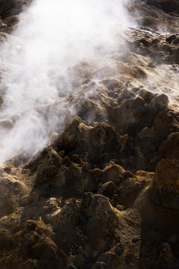 View of geothermal steam rising from the ochre and brown earth creating an otherworldly landscape of textured terrain Hrunamannahreppur Iceland.