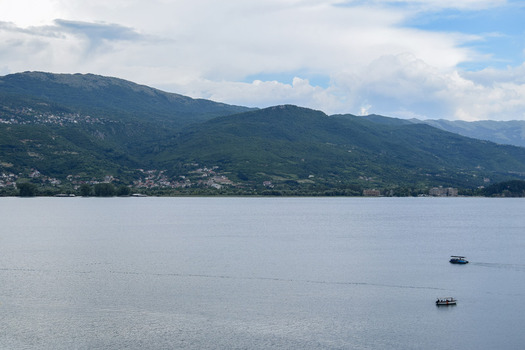 View of Lake Ohrid with small boats on the water and mountains in the background under a cloudy sky in Ohrid Municipality of Ohrid North Macedonia. View of Lake Ohrid with small boats on the water and mountains in the background under a cloudy sky in Ohrid Municipality of Ohrid North Macedonia.