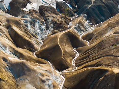 Aerial view of sinuous white streams carving through the ochre and brown earth contrasting with the stark white glacier Landmannalaugar Iceland.