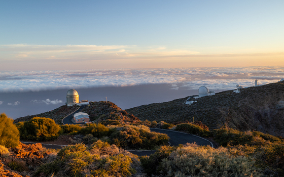 View of Roque de Los Muchachos Astrophysical Observatory with white telescope domes on a rocky mountain ridge above a sea of clouds at sunset Canarias Spain. View of Roque de Los Muchachos Astrophysical Observatory with white telescope domes on a rocky mountain ridge above a sea of clouds at sunset Canarias Spain.