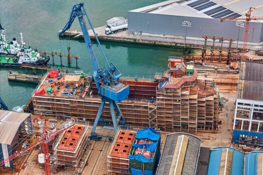 Pasai Donibane Spain 09 March 2026 Aerial view of Puerto Pasajes shipyard with a large blue crane and a ship hull under construction near industrial buildings. Pasai Donibane Spain 09 March 2026 Aerial view of Puerto Pasajes shipyard with a large blue crane and a ship hull under construction near industrial buildings.
