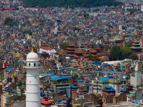 Aerial view of the white Dharahara tower rising above the dense urban landscape with traditional pagoda style temples and residential rooftops in Nepal.