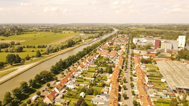 Aerial view of Saint Omer featuring a canal beside residential houses with red tiled roofs surrounded by green fields and industrial buildings in Saint Omer Hauts de France France. Aerial view of Saint Omer featuring a canal beside residential houses with red tiled roofs surrounded by green fields and industrial buildings in Saint Omer Hauts de France France.