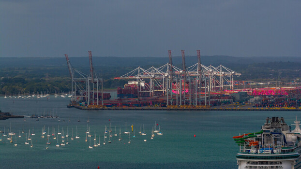 Aerial view of the busy Port of Southampton with container cranes cargo ships and a cruise ship docked surrounded by sailboats in the water in Southampton England United Kingdom. Aerial view of the busy Port of Southampton with container cranes cargo ships and a cruise ship docked surrounded by sailboats in the water in Southampton England United Kingdom.