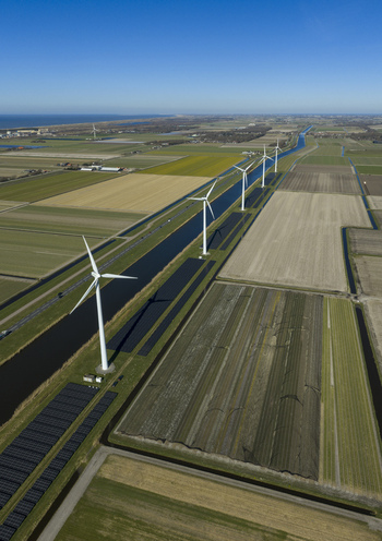 Aerial view of wind turbines standing along a straight canal amidst vast agricultural fields and solar panels under a clear blue sky Netherlands. Aerial view of wind turbines standing along a straight canal amidst vast agricultural fields and solar panels under a clear blue sky Netherlands.