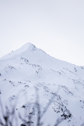 View of a snow covered mountain peak with rocky outcrops under an overcast winter sky in Ersfjord Troms Norway. View of a snow covered mountain peak with rocky outcrops under an overcast winter sky in Ersfjord Troms Norway.