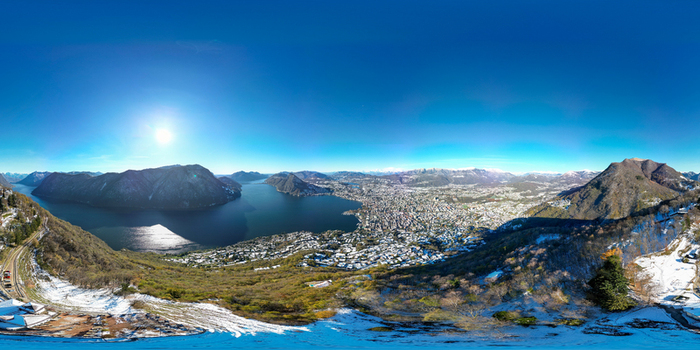 Aerial view of the city of Lugano and Lake Lugano surrounded by snow covered mountains under a clear blue sky Lugano Ticino Switzerland.