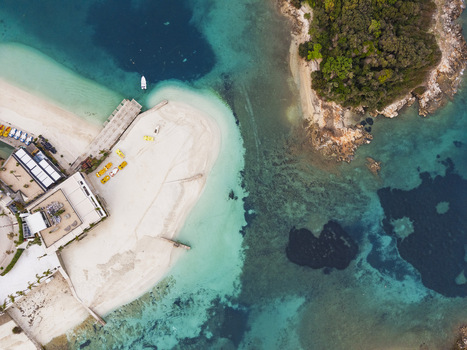Aerial view of the sandy beach and turquoise waters of Ksamil with small boats docked at the pier and lush green islands nearby in Ksamil Vlore County Albania. Aerial view of the sandy beach and turquoise waters of Ksamil with small boats docked at the pier and lush green islands nearby in Ksamil Vlore County Albania.
