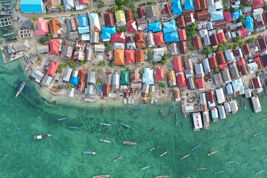 Aerial view of Pulau Maginti a coastal village with colorful rooftops and wooden houses surrounded by small boats in the clear turquoise water of Maginti South East Sulawesi Indonesia.