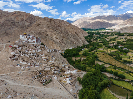 Aerial view of Thiksey Monastery perched on a hillside with traditional white buildings surrounded by arid mountain slopes and a lush green valley in Ladakh Division Ladakh India. Aerial view of Thiksey Monastery perched on a hillside with traditional white buildings surrounded by arid mountain slopes and a lush green valley in Ladakh Division Ladakh India.