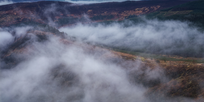 Aerial view of thick mist and low clouds rolling over the rugged hills and dense evergreen forests of Glendalough County Wicklow Ireland.