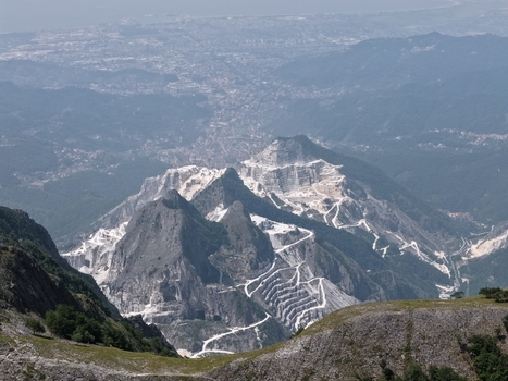 Aerial view of the Carrara marble quarries with white stone terraces winding access roads and rugged mountain slopes in Carrara Tuscany Italy. Aerial view of the Carrara marble quarries with white stone terraces winding access roads and rugged mountain slopes in Carrara Tuscany Italy.