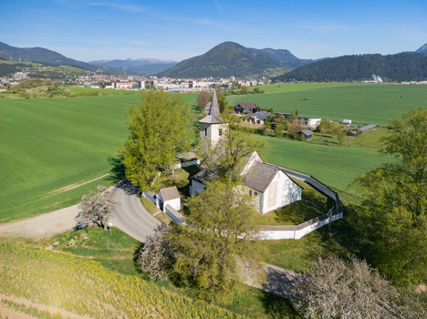 Aerial view of the All Saints Church in Ludrova surrounded by lush green fields stone walls and rolling hills under a clear blue sky Ludrova Zilina Region Slovakia. Aerial view of the All Saints Church in Ludrova surrounded by lush green fields stone walls and rolling hills under a clear blue sky Ludrova Zilina Region Slovakia.