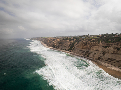 Aerial view of the rugged cliffs and breaking waves along the sandy coastline under a cloudy sky in San Diego California United States. Aerial view of the rugged cliffs and breaking waves along the sandy coastline under a cloudy sky in San Diego California United States.