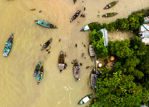 Aerial view of Baish Mowza Sarak Bazar with numerous small wooden boats carrying people navigating the river surrounded by lush trees in Nabinagar Chittagong Division Bangladesh. Aerial view of Baish Mowza Sarak Bazar with numerous small wooden boats carrying people navigating the river surrounded by lush trees in Nabinagar Chittagong Division Bangladesh.