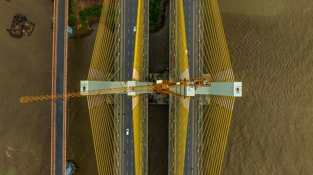 Aerial view of the Zuari Bridge with its distinctive yellow cables and a construction crane positioned over the river in Cortalim Goa India.