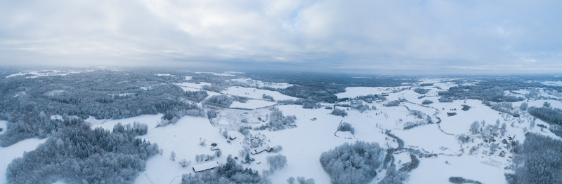 Aerial view of snow covered landscape with dense forests open fields and scattered rural buildings under a cloudy winter sky in Latvia. Aerial view of snow covered landscape with dense forests open fields and scattered rural buildings under a cloudy winter sky in Latvia.