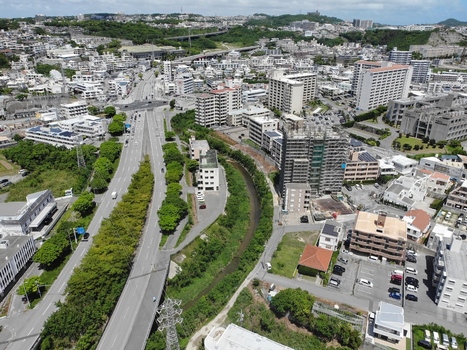 Aerial view of the urban landscape in Haebaru featuring residential apartment buildings a winding canal and roads surrounded by lush greenery in Haebaru Okinawa Japan.