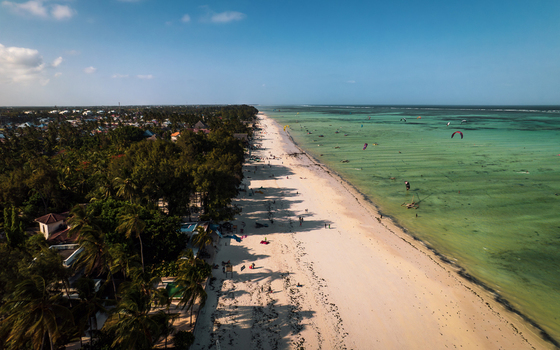 Aerial view of the vibrant turquoise ocean meeting the soft sandy beach as kitesurfers dance on the waves near the shore Paje Tanzania. Aerial view of the vibrant turquoise ocean meeting the soft sandy beach as kitesurfers dance on the waves near the shore Paje Tanzania.