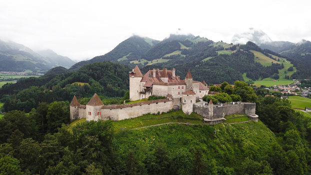 Aerial view of Chateau de Gruyeres on a lush green hill surrounded by dense forests and misty Alpine mountains Gruyeres Fribourg Switzerland.