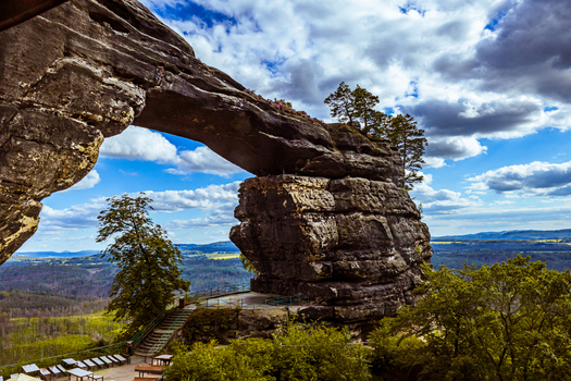 View of Pravcicka Brana the largest natural sandstone arch in Europe with lush green trees and a dramatic cloudy blue sky in Hrensko Usti nad Labem Region Czechia.