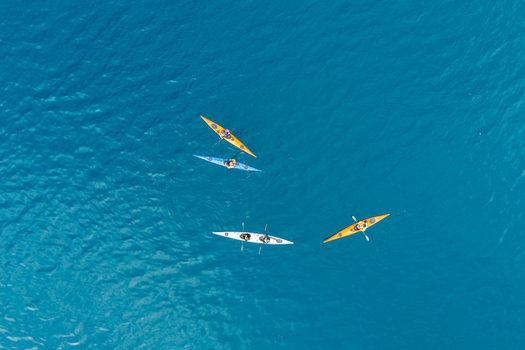 Aerial view of four colorful kayaks paddling on the deep blue waters of the Arctic sea near Uummannaq Kitaa Greenland. Aerial view of four colorful kayaks paddling on the deep blue waters of the Arctic sea near Uummannaq Kitaa Greenland.