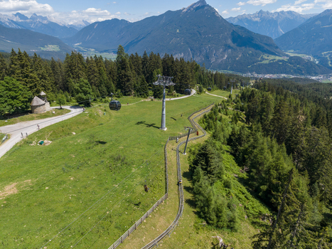 Aerial view of a cable car and a summer toboggan run winding through green alpine meadows and pine forests in the mountains of Imst Tyrol Austria.